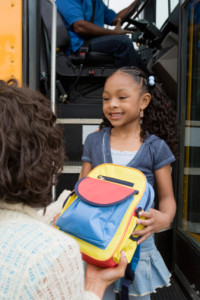 Mother Handing Daughter Backpack on School Bus