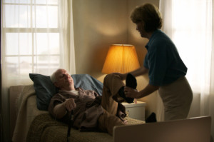 elderly caucasian man in a brown robe lays in bed and gets some physical therapy from a home nurse