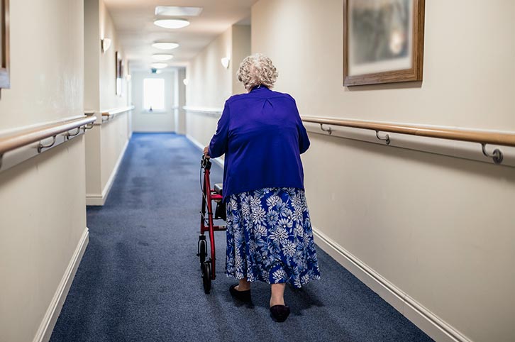 elderly woman using a walker in a carpeted hallway