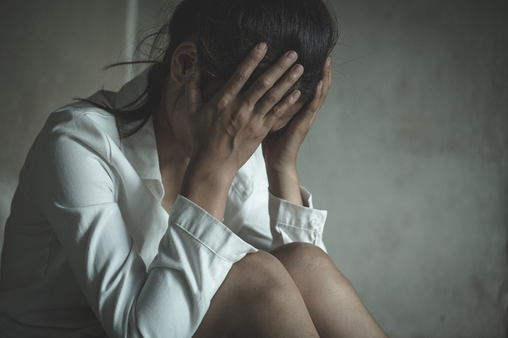 woman sits with hands over her face