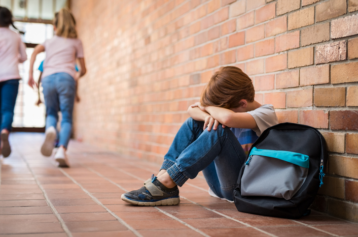 boy sits alone on floor of a school hallway