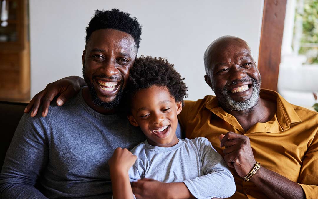 man and his senior dad and young son laughing together on a sofa