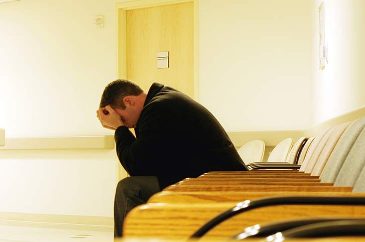 man in a hospital hallway with head in his hands